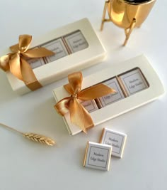 two white boxes with gold bows and labels on them, next to a golden cup