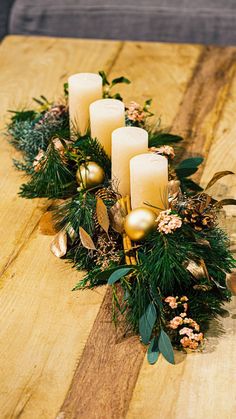 candles are arranged on a wooden table with greenery and pine cones in the center