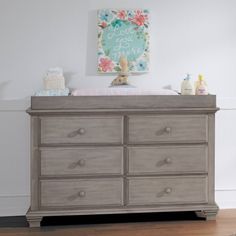 a baby's room with a gray dresser and white walls