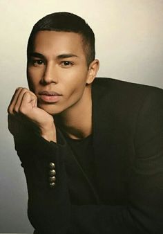 a man sitting down with his hand on his chin and looking at the camera while wearing a black shirt