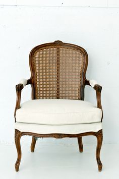 an old wooden chair with white cushions against a white wall, in front of a brick wall