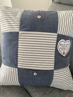 a blue and white striped pillow with a heart patch on the front, sitting on a gray couch