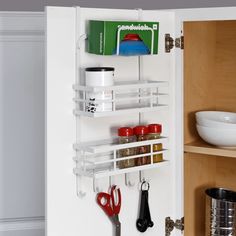 a kitchen cabinet door is open with spices and scissors hanging on the wall next to it