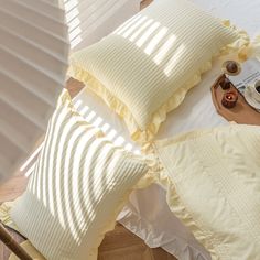 a bed with yellow ruffles and pillows on top of it, next to an alarm clock