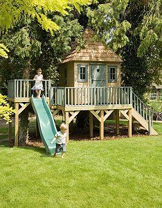 two children playing on a slide in the grass near a tree house with a deck