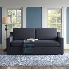 a living room with blue walls and wood flooring is pictured in this image, the couch has a throw blanket on it