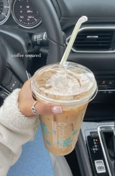 a person holding up a cup with a straw in their hand and steering wheel behind them