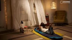 a woman laying on the floor in front of a window with white curtains and lights