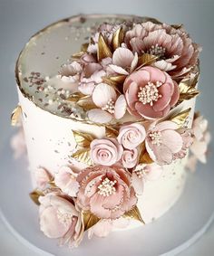 a three tiered cake decorated with pink flowers and gold leaf accents on a white plate