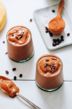 three spoons with chocolate pudding on them sitting next to bananas and raisins