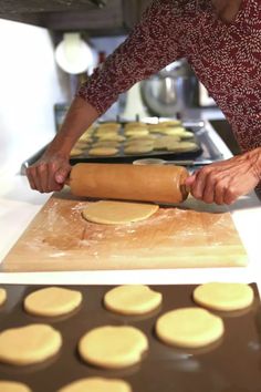 a woman rolling out dough on top of a wooden board next to a cookie sheet