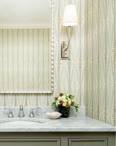 a bathroom vanity with marble counter top and wallpapered walls in the back ground