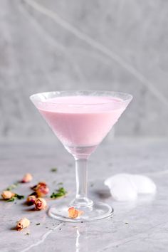 a pink drink in a martini glass with rose petals on the side