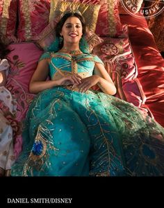 a woman laying on top of a bed in a blue and green dress with gold trim