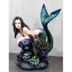 a figurine of a mermaid with a turtle on her lap sitting on a rock