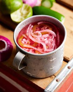 a metal pot filled with red onions on top of a wooden cutting board next to green peppers