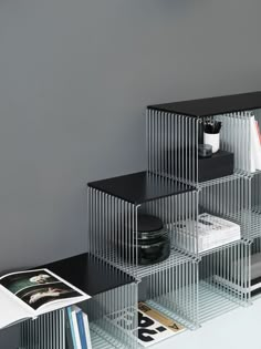 three metal shelves with magazines and books on top of each other in front of a gray wall