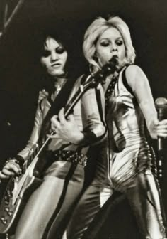 two women are performing on stage with microphones in their hands and one is holding a guitar