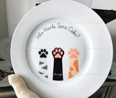 a white plate with black and orange paw prints on it, which says who wants some cake?