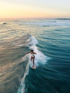 a woman riding a surfboard on top of a wave in the ocean at sunset