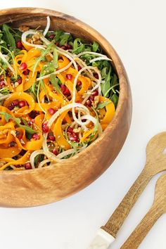 a salad in a wooden bowl with greens and oranges on the side next to a fork