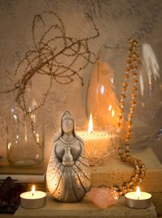 a statue sitting on top of a wooden table next to candles and glass vases