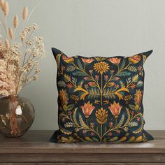 a decorative pillow sitting on top of a wooden table next to a vase with dried flowers