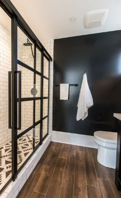 a bathroom with black walls and white tile on the floor, along with wooden floors