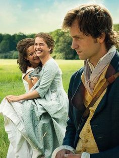 two women and a man are sitting on the grass in front of a green field