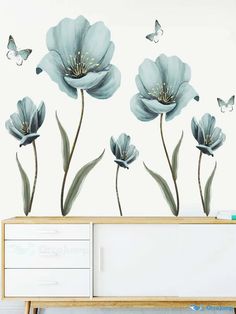 blue flowers and butterflies on a white wall in a living room with a wooden dresser