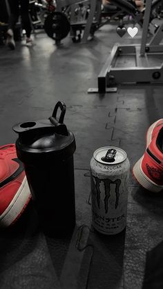 a pair of red shoes sitting on top of a gym floor next to a can of beer