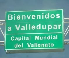 a green street sign hanging from the side of a metal pole in front of a blue sky