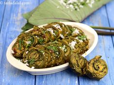 there are some artichokes in a white bowl next to a green leaf