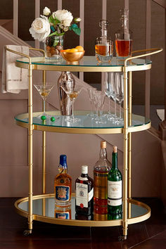 a gold bar cart with wine glasses and liquor bottles on the bottom shelf next to a stair case