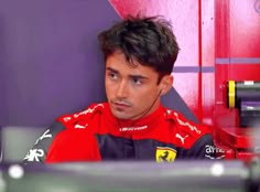 a man sitting in front of a computer monitor wearing a red and black suit with the ferrari logo on it