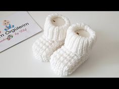 a pair of white knitted baby booties sitting on top of a table next to a sign