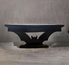 a black table with a bat design on it's top and bottom, in front of a gray wall