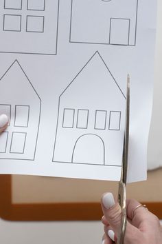 a person cutting paper with scissors in front of a house cut out on a piece of paper