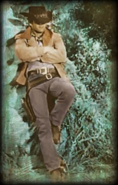 a man with his arms crossed leaning against a wall wearing a cowboy hat and jeans