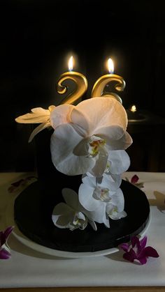 a black hat with white orchids and candles on it is sitting on a table