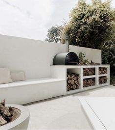 an outdoor kitchen with firewood stacked on the shelves and in front of it is a bbq