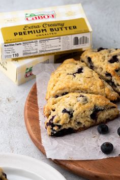 two blueberry scones sitting on top of a cutting board next to a carton of cream