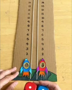 a person is holding two magnets in front of a cardboard board with numbers and rockets on it