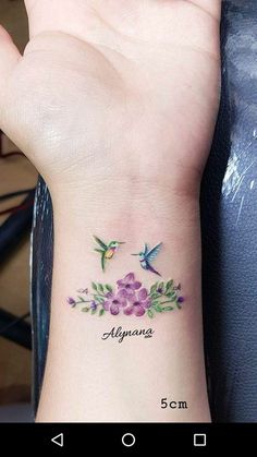 a small wrist tattoo with two hummings and flowers on the left side of the wrist