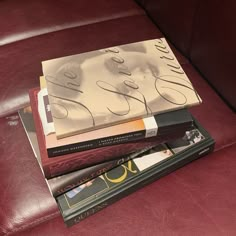 a stack of books sitting on top of a red leather couch next to each other