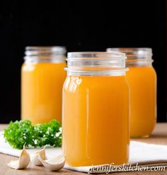 three jars filled with orange liquid sitting on top of a table next to garlic and parsley