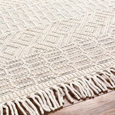 an area rug with fringes on top of wooden flooring next to a wood table