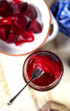 a spoon with some red food in it next to a bowl full of beets