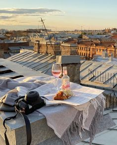 two glasses of wine are sitting on a table with food and drinks in front of the city skyline