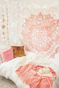 a white bed topped with pink pillows and blankets next to a wall covered in lights